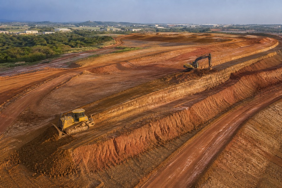 Vista aérea de terreno em terraplanagem com trator de esteira e escavadeira executando platôs em solo laterítico